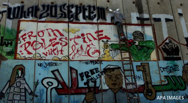 Foreign activist paints graffiti on a separation barrier during a protest calling for a Palestinian state with full UN membership at the Qalandia checkpoint between the West Bank city of Ramallah and Jerusalem, Saturday,...