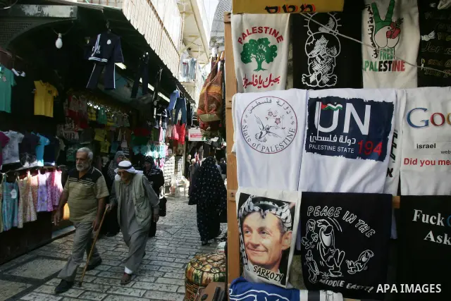 Palestinians walk past a souvenir shop in Jerusalem's Old City displaying T-shirts with pictures of French President Nicolas Sarkozy wearing the traditional Arab headdress keffiyeh, as a group of Jews touring a Jerusalem...