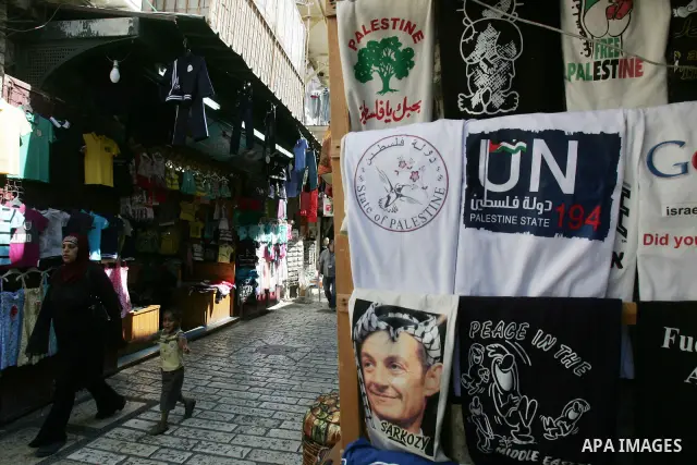Palestinians walk past a souvenir shop in Jerusalem's Old City displaying T-shirts with pictures of French President Nicolas Sarkozy wearing the traditional Arab headdress keffiyeh, as a group of Jews touring a Jerusalem...
