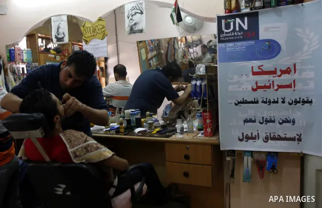 A Palestinian hairdresser cuts customer's hair near a poster of support of the UN bid for palestinian statehood, in the southern Gaza Strip Rafah refugee camp on September 18, 2011. The Islamist Hamas movement said the U...