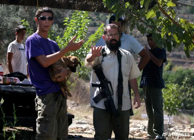 An armed Israeli settler from the Halamish settlement looks at members of pro-Palestinian volunteer-based campaign which will intervene and respond to cases of violence towards Palestinians by Jewish settlers in the West...
