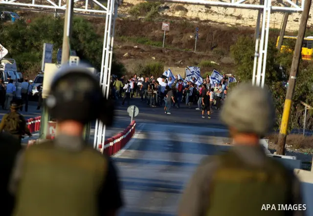 Israeli soldiers keep watch as Jewish settlers hold Israeli flags during a protest against the Palestinian bid for statehood at the United Nations on September 20 , 2011, close at the Jewish settlement of Beit El, in the...
