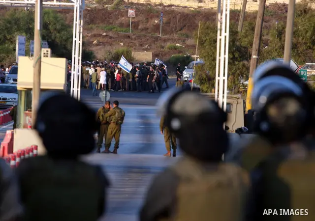 Israeli soldiers keep watch as Jewish settlers hold Israeli flags during a protest against the Palestinian bid for statehood at the United Nations on September 20 , 2011, close at the Jewish settlement of Beit El, in the...