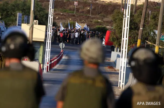 Israeli soldiers keep watch as Jewish settlers hold Israeli flags during a protest against the Palestinian bid for statehood at the United Nations on September 20 , 2011, close at the Jewish settlement of Beit El, in the...