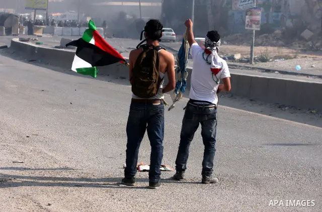A Palestinian protester waves his national flag in front of Israeli soldiers during clashes at the Qalandia checkpoint between the West Bank city of Ramallah and Jerusalem, Wednesday, Sept. 21, 2011. Palestinians clashed...