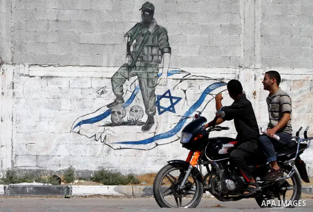 Palestinians ride motorcycle past a graffiti depicting a Palestinian militant stepping on skulls and the Israeli flag in Gaza City, Saturday, Sept. 28, 2011 as Palestinians mark the 11th anniversary of Al-Aqsa Intifada (...
