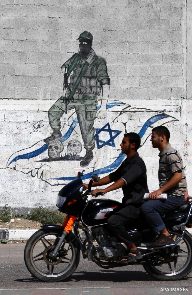 Palestinians ride motorcycle past a graffiti depicting a Palestinian militant stepping on skulls and the Israeli flag in Gaza City, Saturday, Sept. 28, 2011 as Palestinians mark the 11th anniversary of Al-Aqsa Intifada (...
