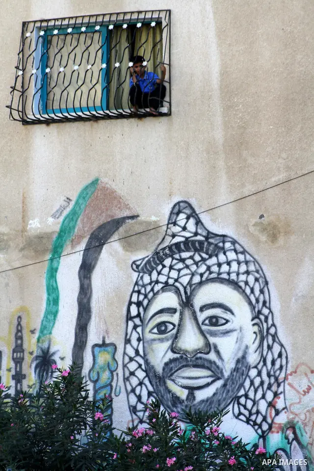 A Palestinian child sits on a window above a graffiti depicting the late Palestinian president Yasser Arafat in Gaza City, Saturday, Sept. 28, 2011 as Palestinians mark the 11th anniversary of Al-Aqsa Intifada (uprising)...