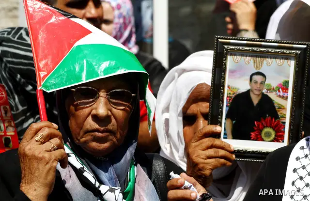 A Palestinian woman covers her head with a Palestinian flag as others hold pictures of relatives held in Israeli jails, during a protest calling for their release, in front of the International Red Cross building in Gaza...