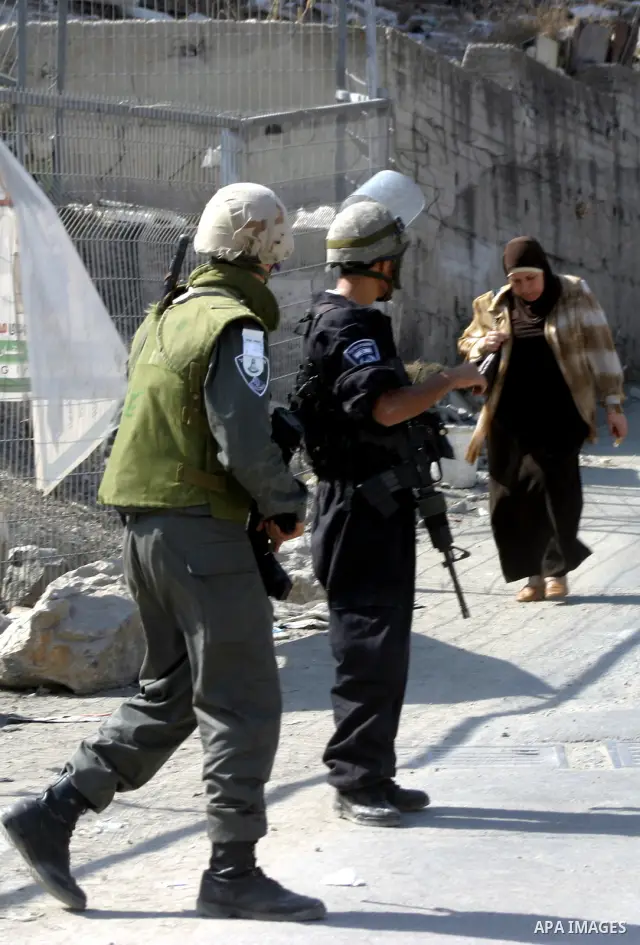 A Palestinian woman walks past Israeli soldiers standing guard in the east Jerusalem neighborhood of Silwan, Thursday, Sept. 29, 2011. Israel on Tuesday approved construction of 1,100 homes for Jews on the annexed land i...