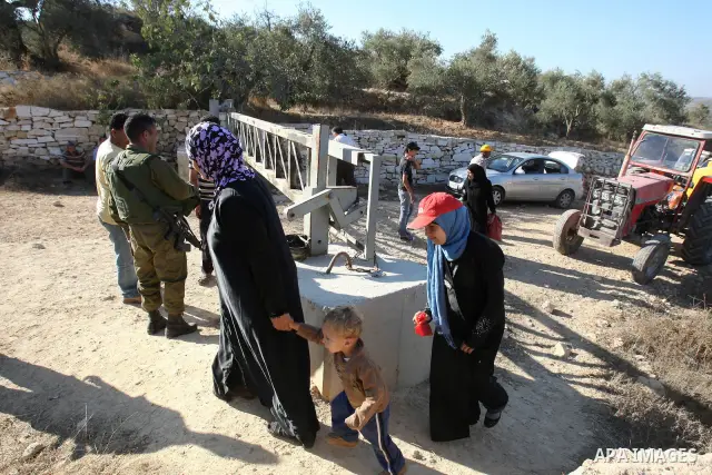 Palestinian farmers cross a barrier erected by Israel on Palestinian land to harvest their olive in groves as Israeli soldiers stand guard at a barrier erected to protect nearby Jewish settlements in the occupied West Ba...