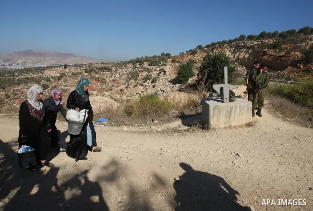 Israeli soldiers stand guard at a barrier erected on Palestinian land to protect nearby Jewish settlements in the occupied West Bank, as Palestinian farmers cross to harvest their olive groves just outside the Palestinia...