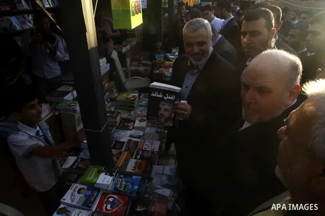 Palestinian Prime Minister in Gaza Strip, Ismail Haniya holds a book with a picture of Hamas leader Khaled Meshaal as he attends the opening ceremony of the book exhibition which organised by the Ministry of Culture in G...
