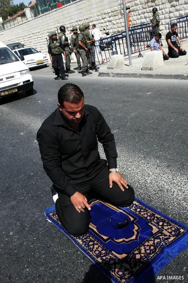 Israeli soldiers stand guard as Palestinian Muslims attend Friday prayers at a street in the neighbourhood of Ras al-Amud, in East Jerusalem (Al-Aqsa Mosque compound in the background) on October 7,2011. Israel limited a...