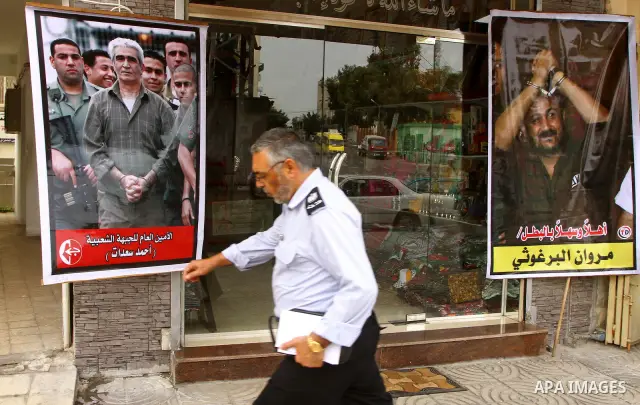 Palestinian Hamas policeman walk past pictures of Ahmed Saadat and Merwan al-Barghouti after a prisoner swap between Hamas and Israel, in Gaza City October 12, 2011. Israelis welcomed on Wednesday a major prisoner swap t...