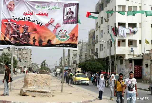Palestinians walk next to a poster for captured Israeli soldier Gilad Shalit in Rafah town in the southern Gaza Strip October 12, 2011. Israelis welcomed on Wednesday a major prisoner swap that will free soldier Gilad Sh...