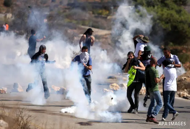 Palestinian, Israeli and foreign activists run away from tear gas canisters fired by Israeli troops during a demonstration against the expansion of the nearby Jewish settlement of Halamish in the West Bank village of Nab...