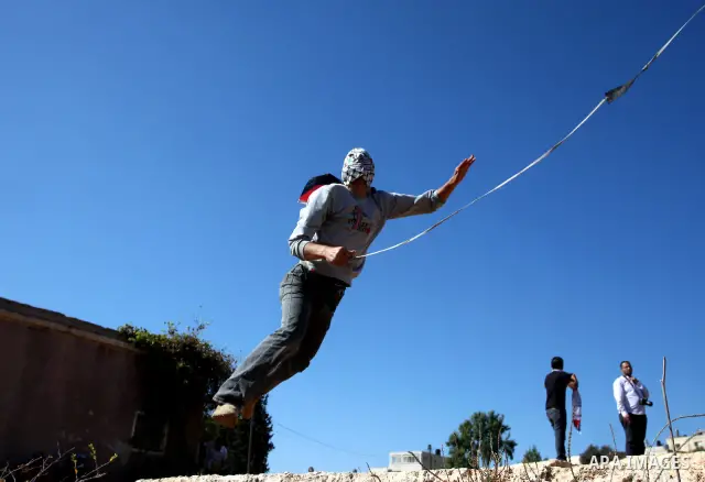 A masked Palestinian demonstrator wields a sling-shot at Israeli troops during a demonstration against the expansion of the nearby Jewish settlement of Halamish in the West Bank village of Nabi Saleh, near Ramallah, Frid...