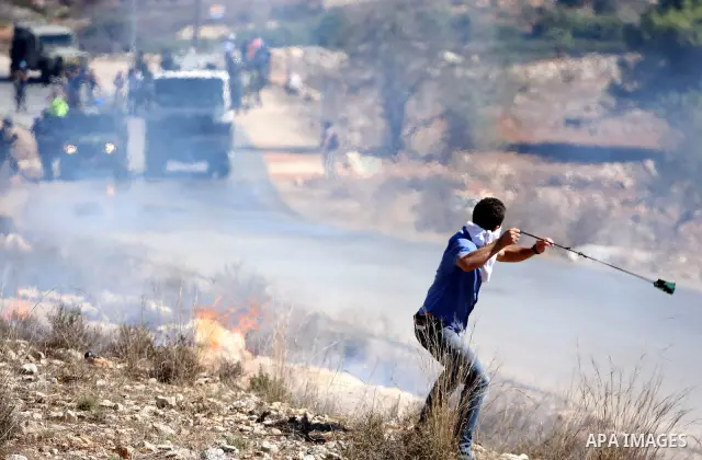 A masked Palestinian demonstrator wields a sling-shot at Israeli troops during a demonstration against the expansion of the nearby Jewish settlement of Halamish in the West Bank village of Nabi Saleh, near Ramallah, Frid...