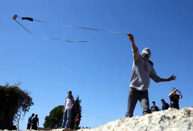 A masked Palestinian demonstrator wields a sling-shot at Israeli troops during a demonstration against the expansion of the nearby Jewish settlement of Halamish in the West Bank village of Nabi Saleh, near Ramallah, Frid...