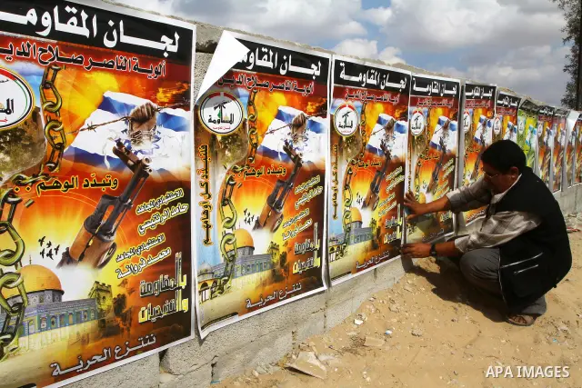 A Palestinian man pastes posters on a wall at the Rafah border crossing in the southern Gaza Strip October 17, 2011, during preparations for the release of prisoners in a swap that is expected to take place on Tuesday. H...
