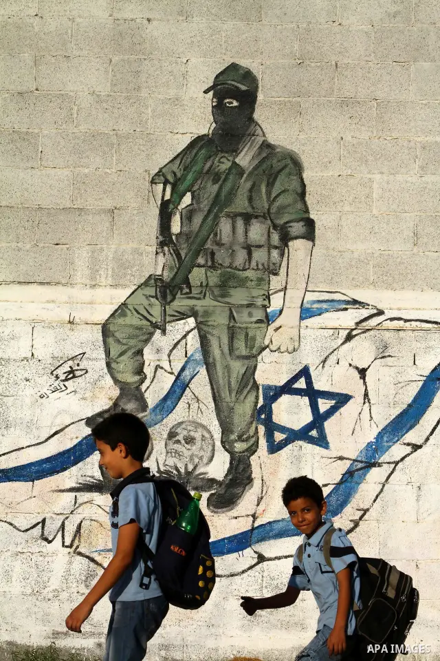 Palestinian boys walk past a graffiti depicting a Palestinian militant stepping on skulls and the Israeli flag in Gaza City, a day before a prisoner swap between Israel and Hamas, Monday, Oct. 17, 2011. Photo by Ashraf A...