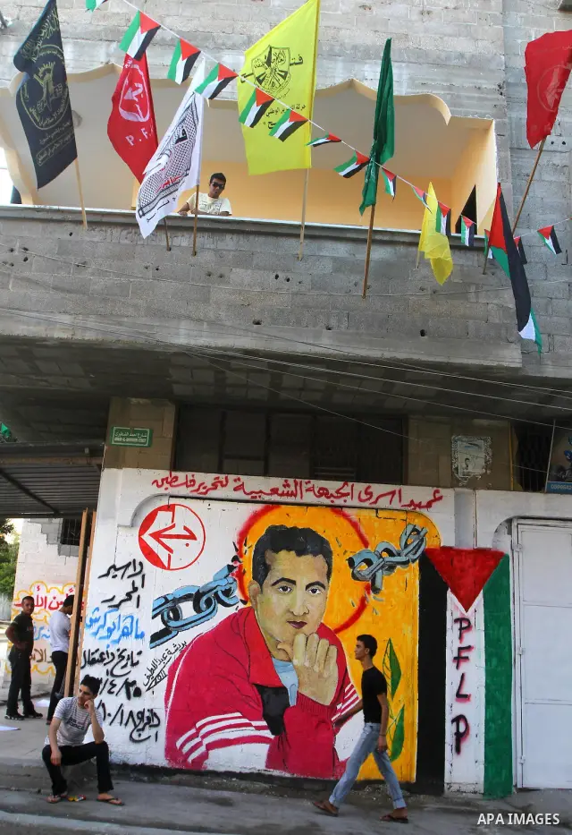 Relatives of Palestinian prisoner, Maher Abu Karesh stand near a graffiti depicting his picture as they gather at his house in the Gaza Strip on 17 October 2011 as they await his release as part of a deal to secure the e...