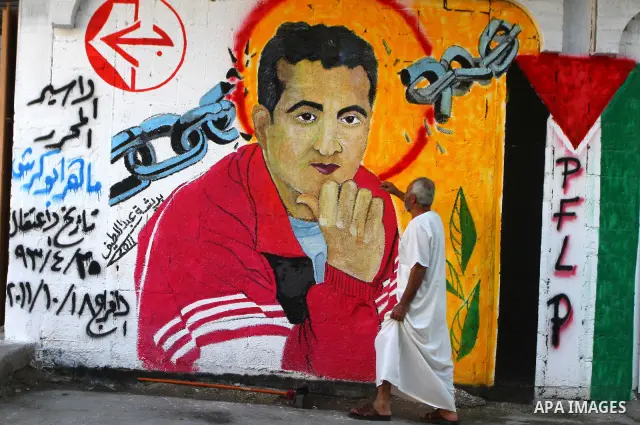Relatives of Palestinian prisoner, Maher Abu Karesh stand near a graffiti depicting his picture as they gather at his house in the Gaza Strip on 17 October 2011 as they await his release as part of a deal to secure the e...