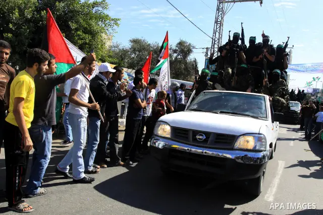 Palestinians keep watch as Hamas militants stand guard in Gaza City on October 18, 2011 as an Israeli-Palestinian prisoner swap deal gets under way. Captive Israeli soldier Gilad Shalit was today freed from five years of...