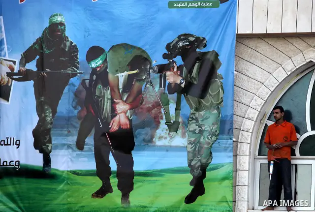 A Palestinian youth stands next a poster showing a Hamas militant carrying an Israeli soldier on the stage erected to welcome Palestinian prisoners released in exchange for the captured Israeli soldier Gilad Schalit in G...