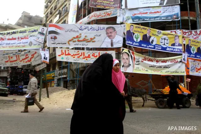 Egyptians walk past electoral campaign banners in Cairo on November 26, 2011 ahead of a three-round parliamentary election. The parliamentary elections that get underway on November 28 will be the first polls since a pop...