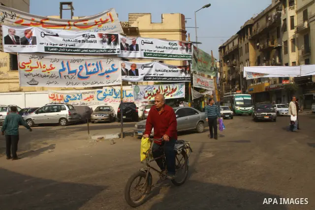 Egyptians walk past electoral campaign banners in Cairo on November 26, 2011 ahead of a three-round parliamentary election. The parliamentary elections that get underway on November 28 will be the first polls since a pop...