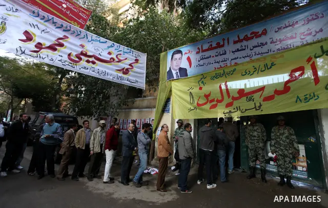 Voters line up outside a polling center beneath campaign posters on the first day of parliamentary elections in Cairo, Egypt, Monday, Nov. 28, 2011. Shaking off years of political apathy, Egyptians on Monday began voting...