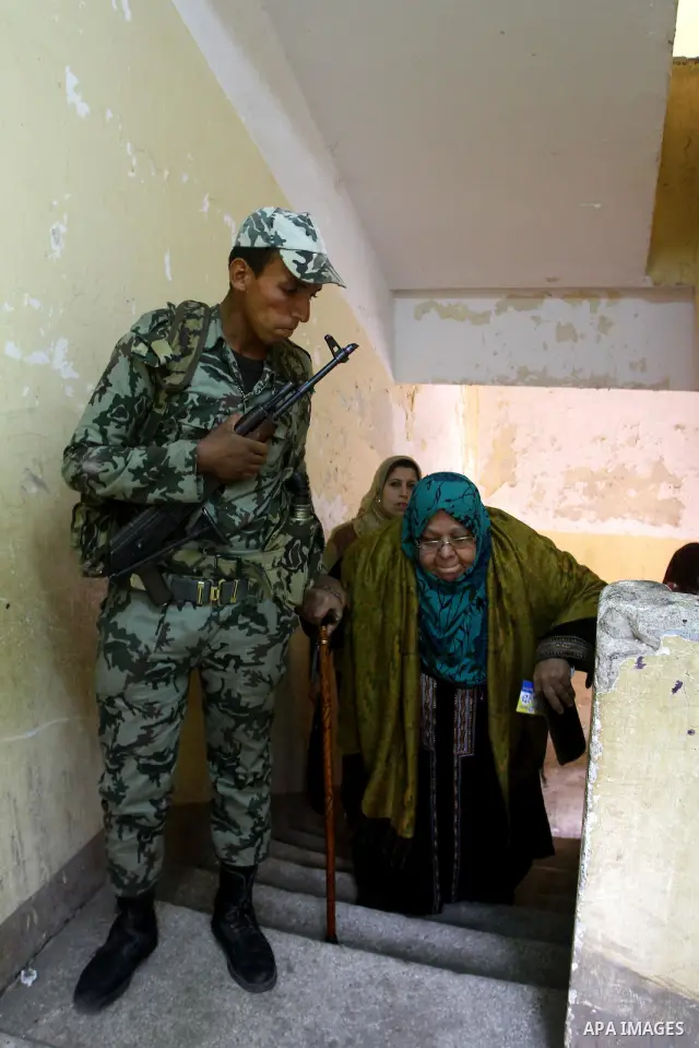 Army soldier helps an Egyptian woman to cast her ballot at a parliamentary polling station in Cairo on November 29, 2011. Egypt hailed the start of its first post-revolution election as a triumph for democracy as more vo...