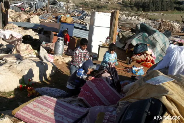 Palestinian Bedouin children collect belongings amidst the rubble of a structure after it was razed by the Israeli army in the West Bank village of Zayem, near Jerusalem November 29, 2011. According to Israeli authoritie...