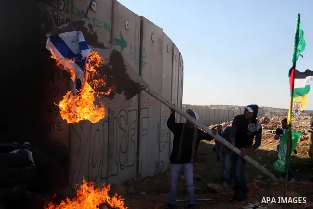 Palestinian protestors set fire the US and Israeli flags during a weekly demonstration near Israel's separation wall in the West Bank village of Nilin, on December 02, 2011. Photo by Issam Rimawi