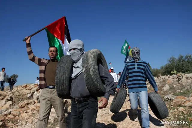 Palestinian protestors clash with Israeli forces standing on the other side of Israel's separation wall during a weekly protest in the West Bank village of Nilin, on December 02, 2011. Photo by Issam Rimawi