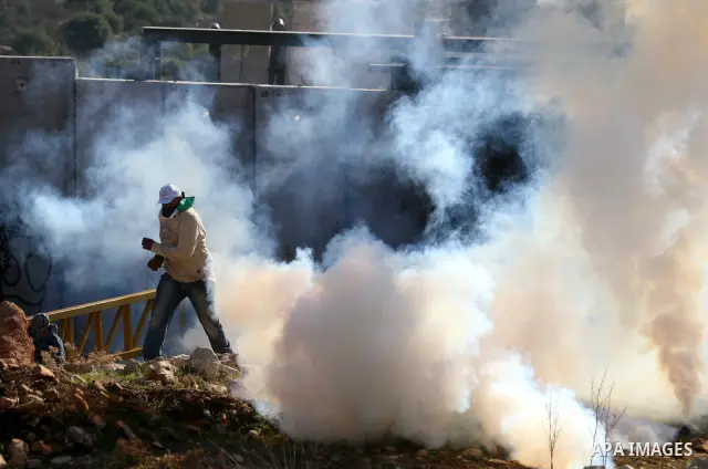 Palestinian protestors clash with Israeli forces standing on the other side of Israel's separation wall during a weekly protest in the West Bank village of Nilin, on December 02, 2011. Photo by Issam Rimawi