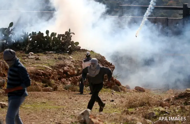 Palestinian protestors clash with Israeli forces standing on the other side of Israel's separation wall during a weekly protest in the West Bank village of Nilin, on December 02, 2011. Photo by Issam Rimawi