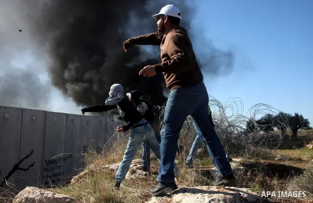 Palestinian protestors clash with Israeli forces standing on the other side of Israel's separation wall during a weekly protest in the West Bank village of Nilin, on December 02, 2011. Photo by Issam Rimawi