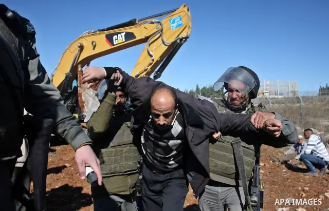 A Palestinian man is carried by Israeli border police officers after he tried to block a construction vehicle from working on Israel's barrier in the West Bank village of Qaladiya near Ramallah December 4, 2011. Accordin...