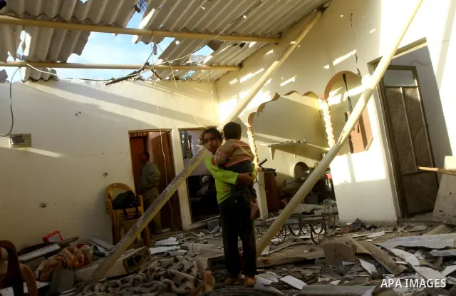 A Palestinian girl holds her brother as she looks at a house damaged in an Israeli air strike in Gaza City December 9, 2011. Violence across the Israeli-Gaza border escalated on Friday with Israeli air strikes killing at...