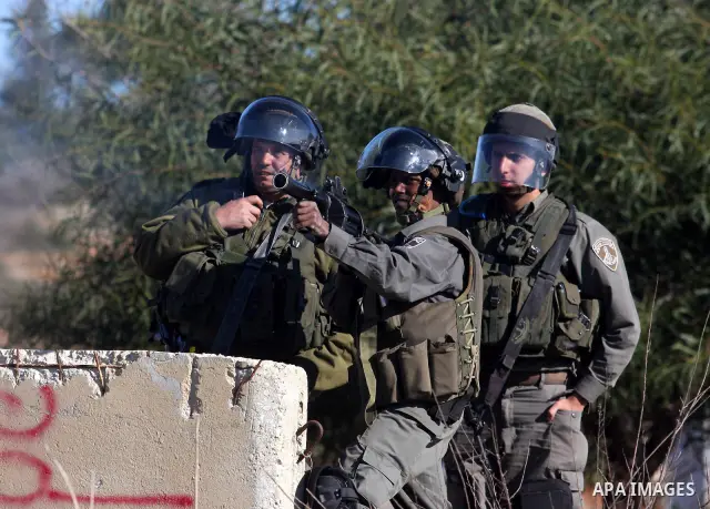 An Israeli soldier fires tear gas towards Palestinian demonstrators during clashes which erupted after the funeral of Palestinian Mustafa Tamimi in the West Bank town of Nabi Saleh, Sunday, Dec. 11, 2011. Tamimi, 28, was...