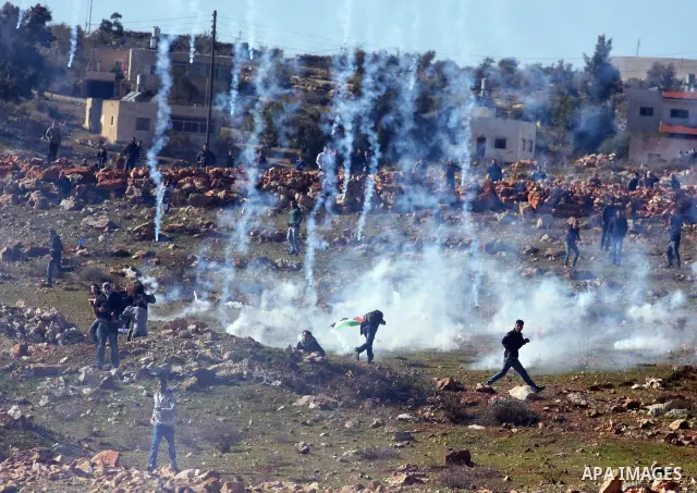 Palestinians try to avoid tear gas fired by Israeli soldiers during clashes which erupted after the funeral of Palestinian Mustafa Tamimi in the West Bank town of Nabi Saleh, Sunday, Dec. 11, 2011. Tamimi, 28, was hurlin...