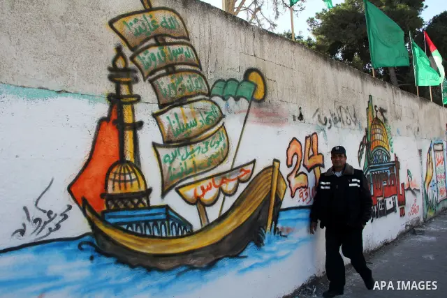 Palestinians walk past a mural depicting slogans for Hamas in the preparation of the anniversary of Hamas Islamic movement foundation in Rafah refugee camp, in southern Gaza Strip on December 11, 2011. Photo by Hatem Oma...