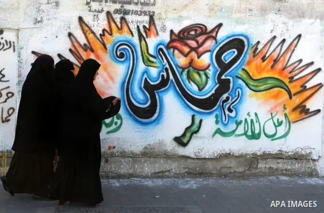 Palestinians walk past a mural depicting slogans for Hamas in the preparation of the anniversary of Hamas Islamic movement foundation in Rafah refugee camp, in southern Gaza Strip on December 11, 2011. Photo by Hatem Oma...