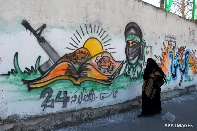 Palestinians walk past a mural depicting slogans for Hamas in the preparation of the anniversary of Hamas Islamic movement foundation in Rafah refugee camp, in southern Gaza Strip on December 11, 2011. Photo by Hatem Oma...