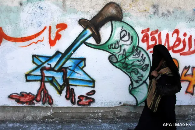 Palestinians walk past a mural depicting slogans for Hamas in the preparation of the anniversary of Hamas Islamic movement foundation in Rafah refugee camp, in southern Gaza Strip on December 11, 2011. Photo by Hatem Oma...