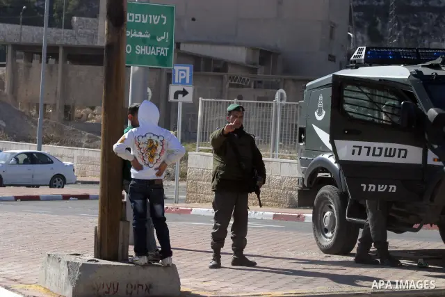 Israeli soldiers stand guard as Palestinians cross through the new opened Israeli checkpoint near the east Jerusalem refugee camp of Shuafat on December 12, 2011. Palestinian youths protested against the construction of...