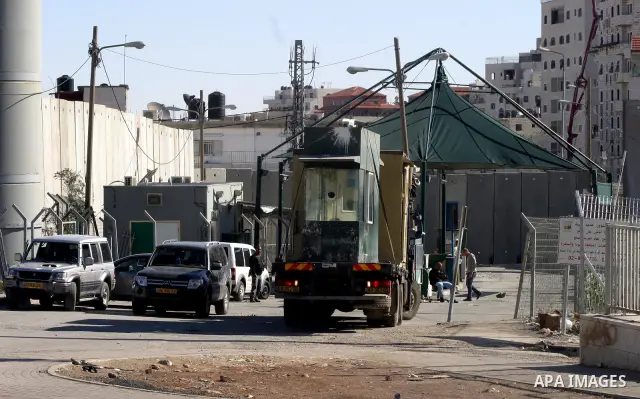Israeli soldiers stand guard as Palestinians cross through the new opened Israeli checkpoint near the east Jerusalem refugee camp of Shuafat on December 12, 2011. Palestinian youths protested against the construction of...